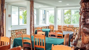 Un restaurante con sillas y mesas de madera, ventanas amplias y una pared de piedra.