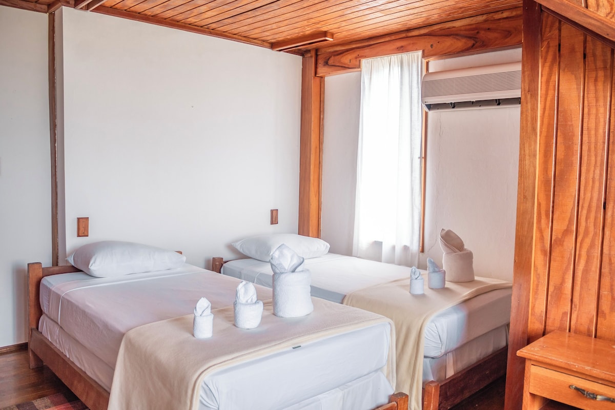 A hotel room with two beds, wooden headboards, white linens, and a wooden ceiling.