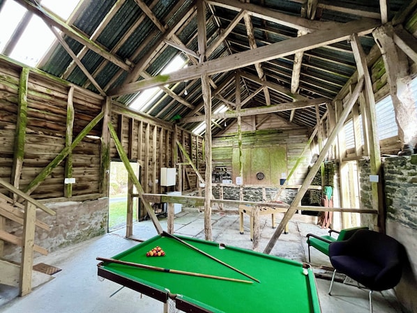 A rustic indoor pool table with a green felt surface, surrounded by wooden beams and stone walls.