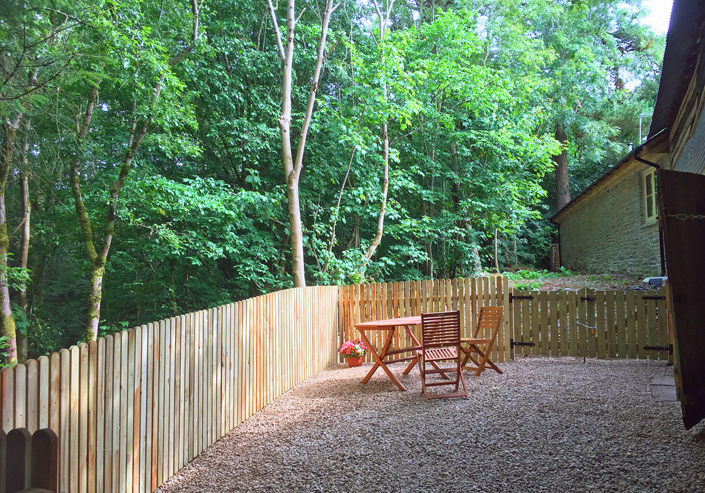 Una terraza de madera con mesa y sillas, rodeada por una valla de madera, ubicada en un área boscosa.
