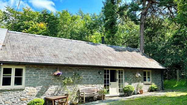 A stone building with a sloped roof, a wooden bench, and a table outside. - Drovers Retreat (Llandrindod Wells)