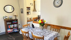 A dining area with a table set for four, surrounded by wooden chairs. A bookshelf filled with books is visible to the left. - Drovers Retreat (Llandrindod Wells)