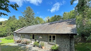 A stone house with a sloped roof, a front porch with a bench, and potted plants. - Drovers Retreat (Llandrindod Wells)