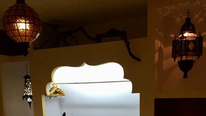 Una habitación acogedora con un estante blanco montado en la pared, una mecedora de madera y una alfombra estampada.