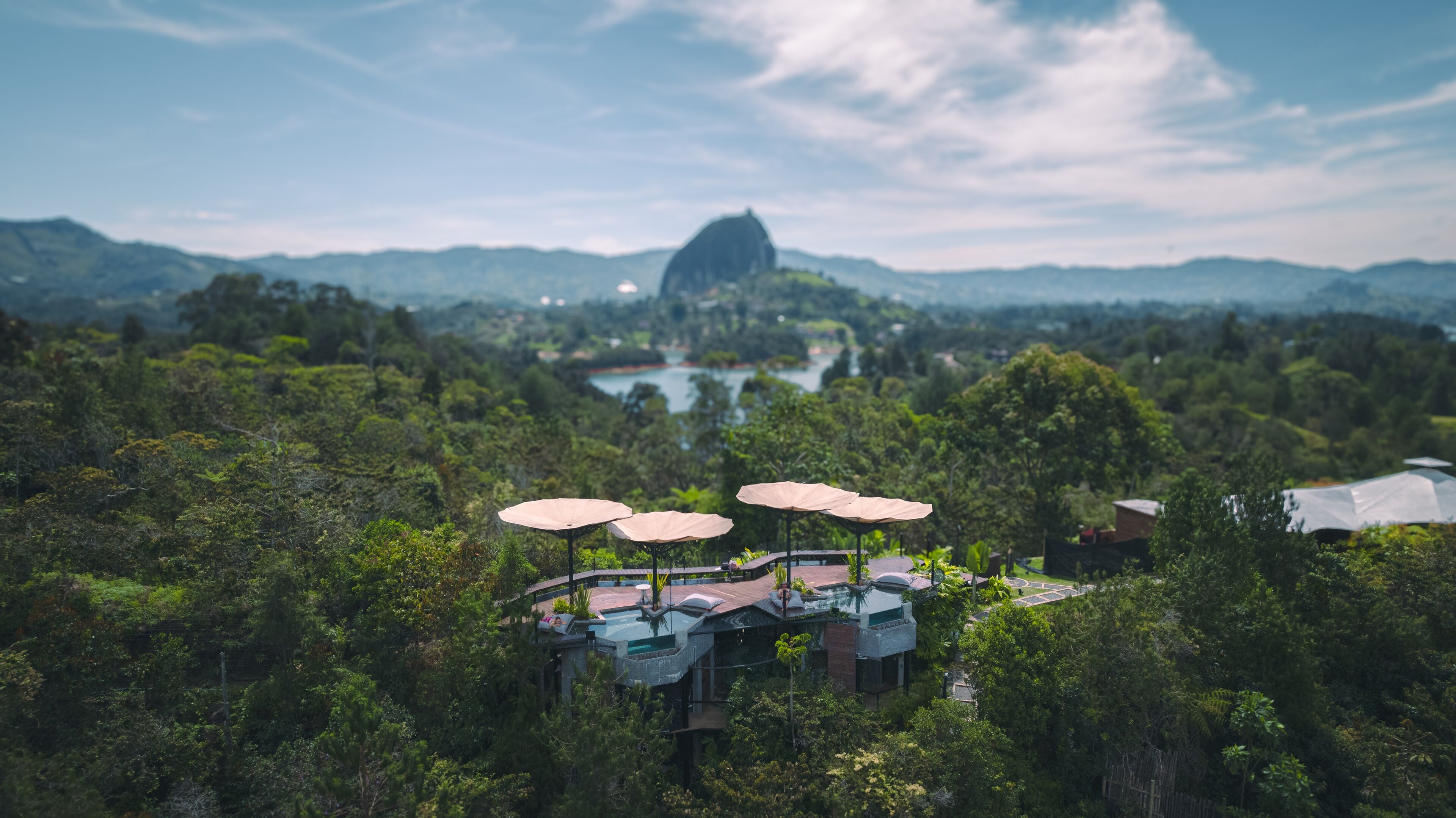 A resort with multiple rooms, some with outdoor umbrellas, surrounded by lush greenery and a lake.