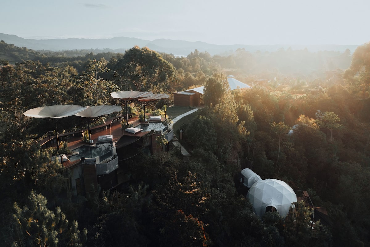 Um resort com área externa para sentar e piscina, rodeado por vegetação exuberante e colinas.