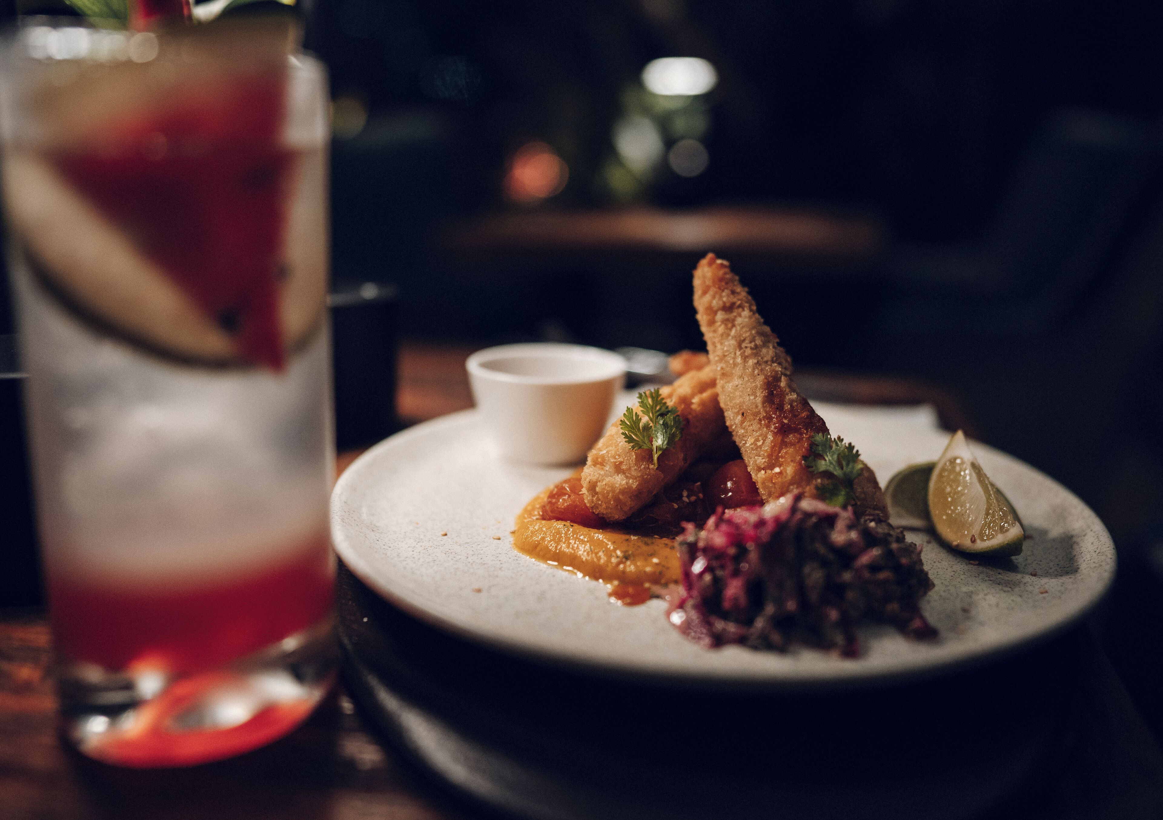A plate of food with breaded items and a side of sauce, accompanied by a glass of drink with a slice of fruit.