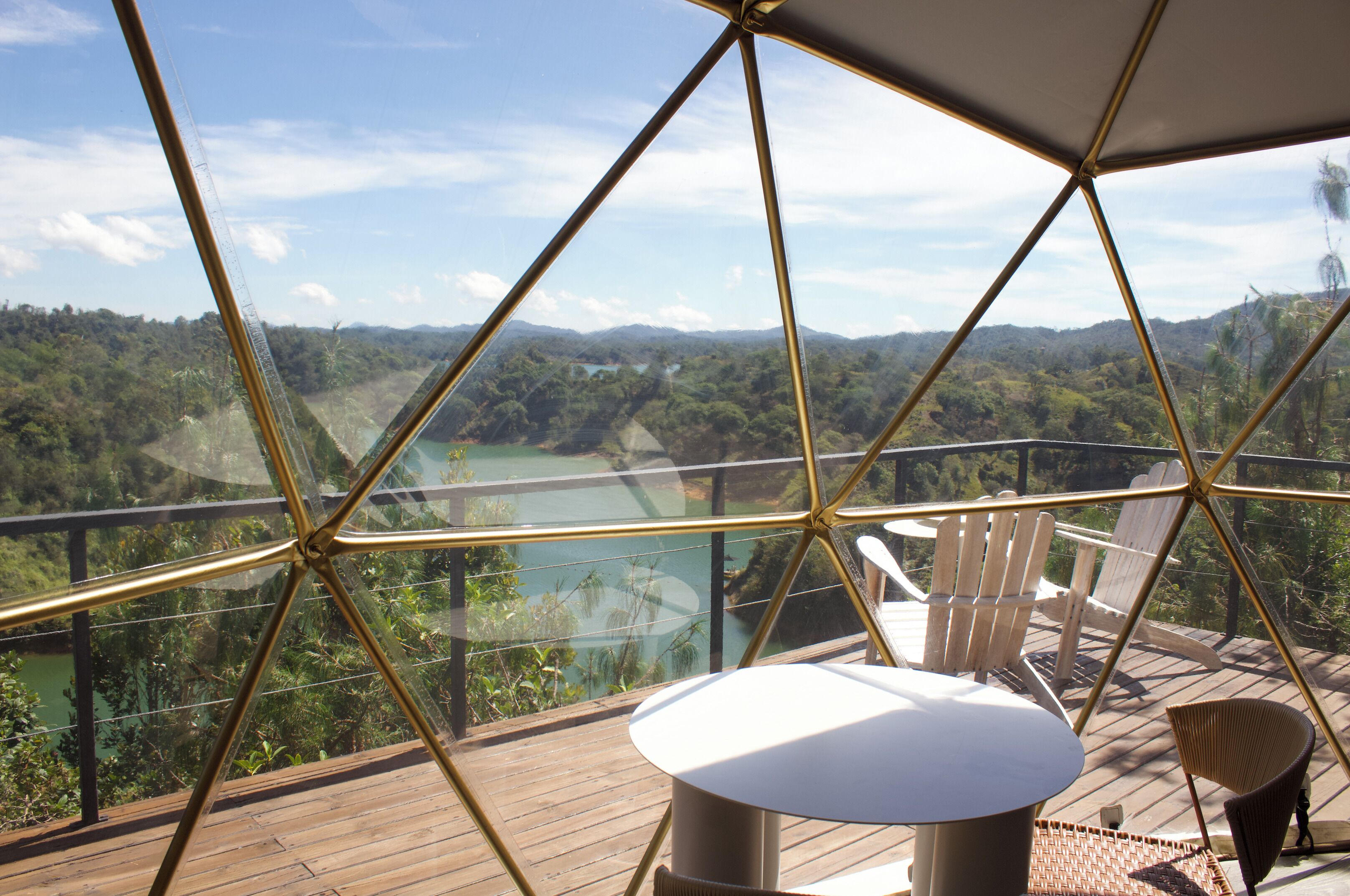 A high vantage point with a clear view of a valley and mountains, a wooden deck, and a glass enclosure with a geometric metal frame.