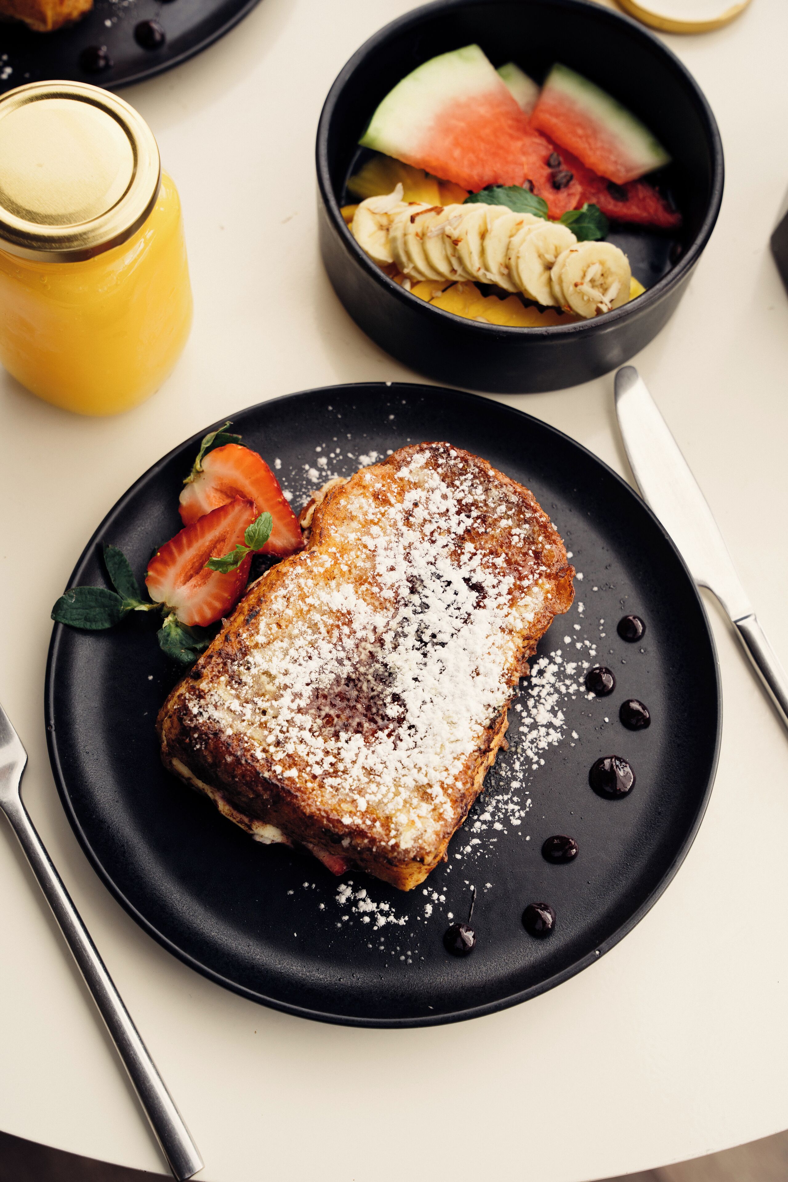 A breakfast plate with French toast, strawberries, and a small bowl of fruit.