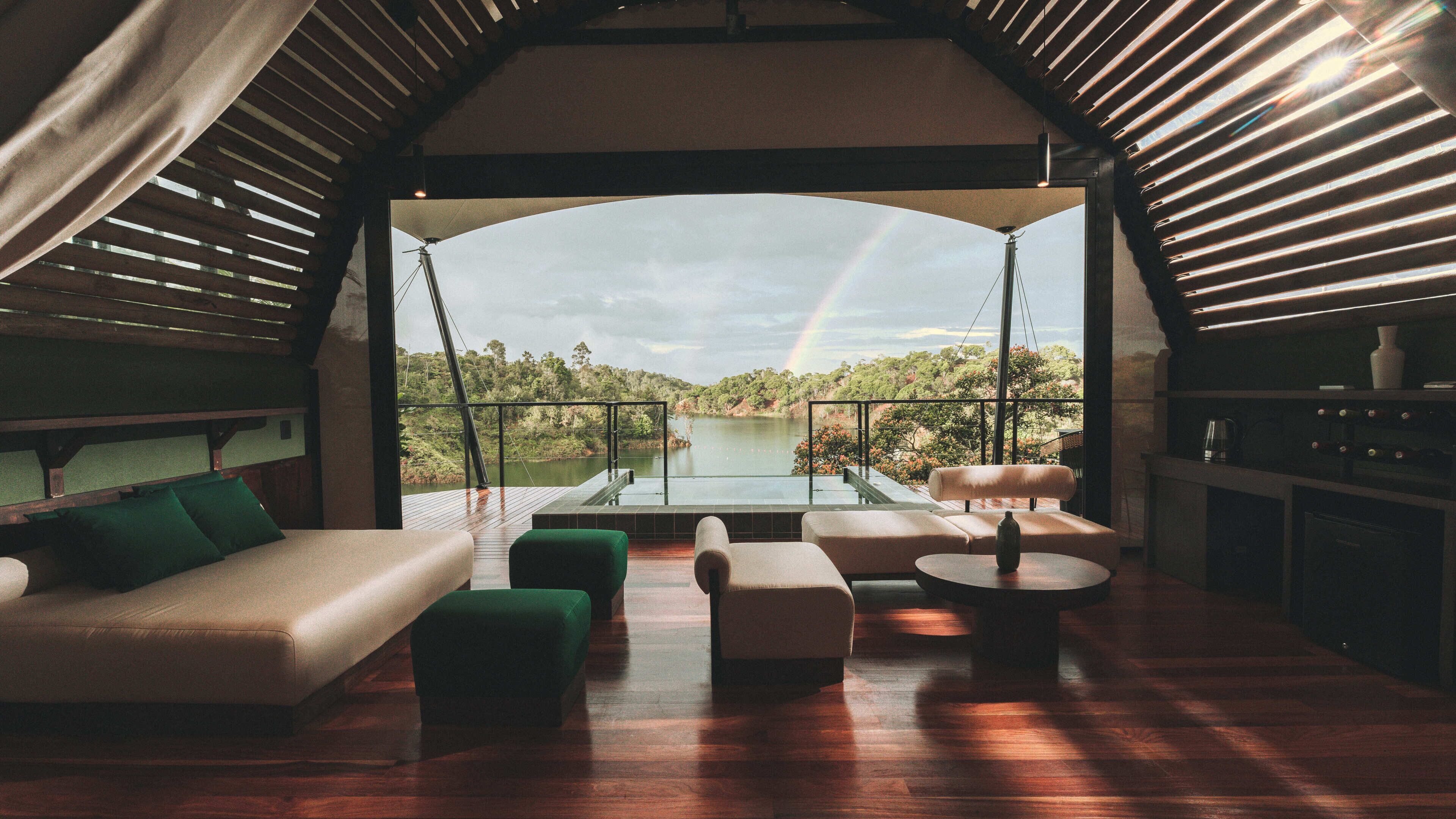 A spacious interior with a wooden floor, a sofa, a round table, and a view of a lake through a large window.