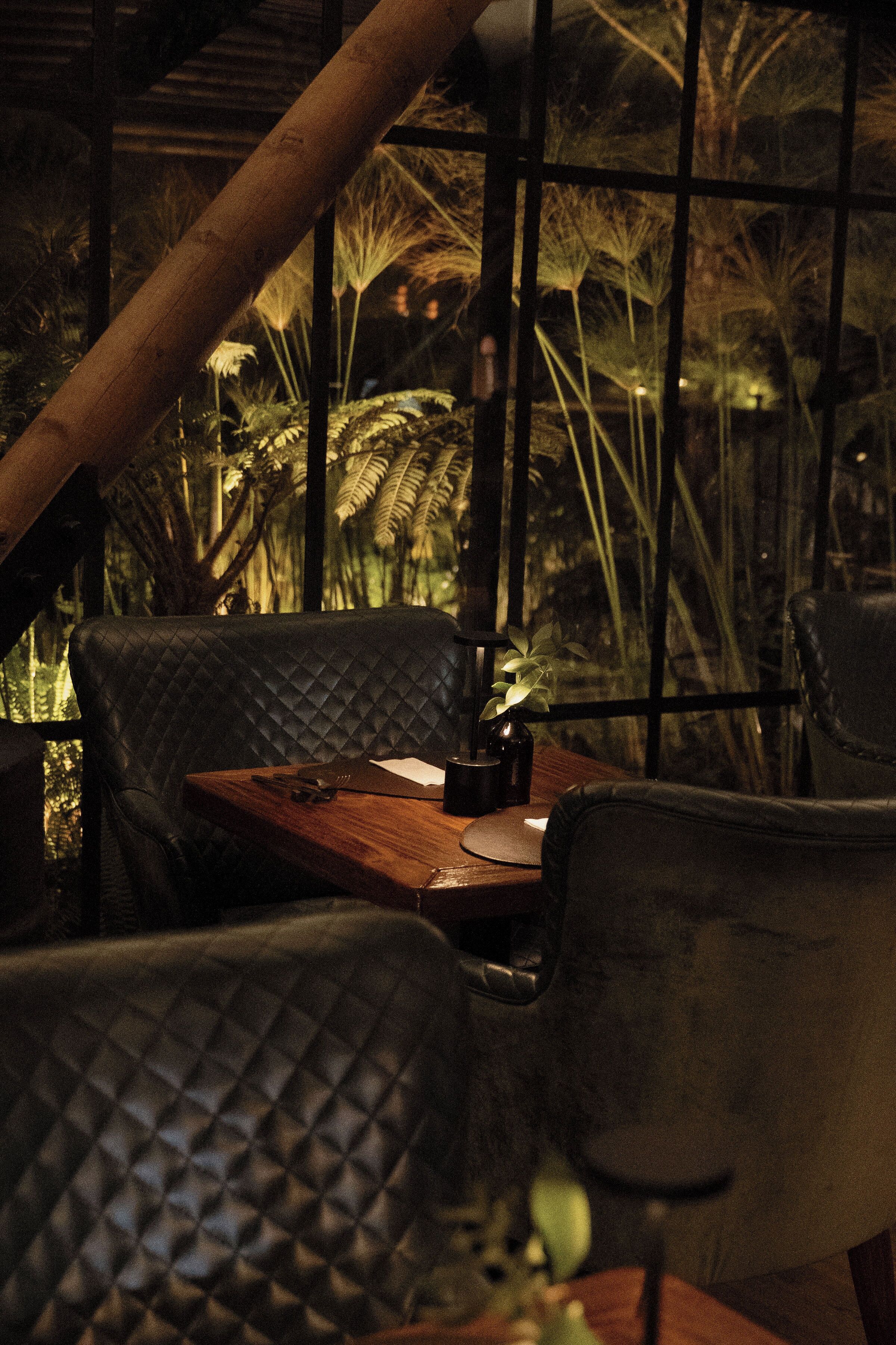 A dimly lit restaurant with a wooden table and black leather chairs.