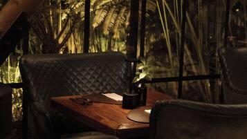 A dimly lit restaurant with a wooden table and black leather chairs.