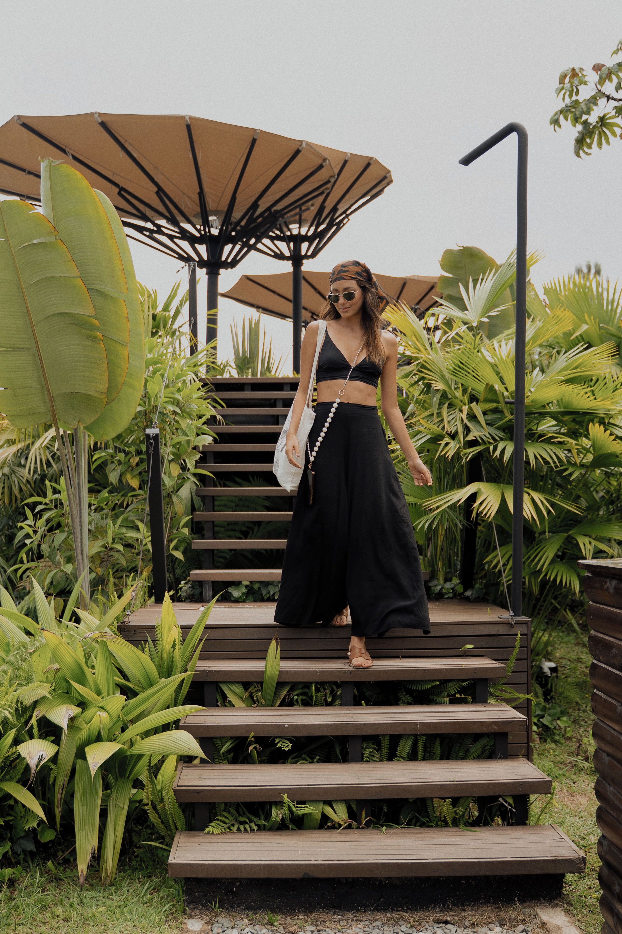 A woman standing on wooden steps surrounded by lush greenery and large umbrellas.