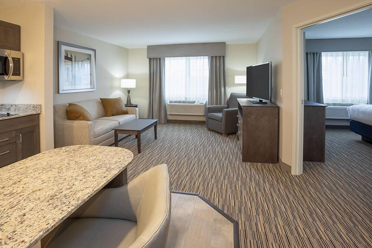 A hotel room with a kitchenette, a sofa, a TV, a desk, and a bed.