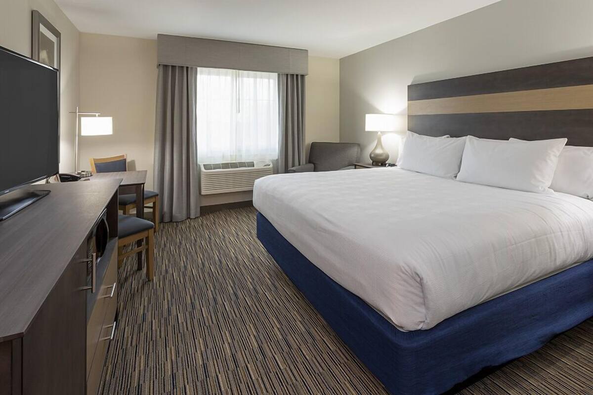 A hotel room with a large bed, a desk with a chair, a television, and a window with curtains.