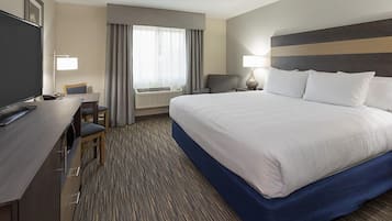 Habitación de hotel con una cama grande, un escritorio con silla, televisión y ventana con cortinas.