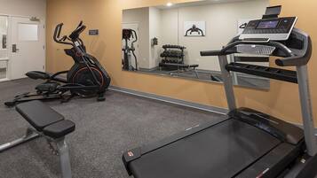 Ein Fitnessraum mit Laufband, Crosstrainer und Bank.