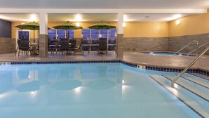 Una piscina interior con agua azul cristalina, rodeada de sillones de descanso y sombrillas, y una escalera de acceso al área de la piscina.