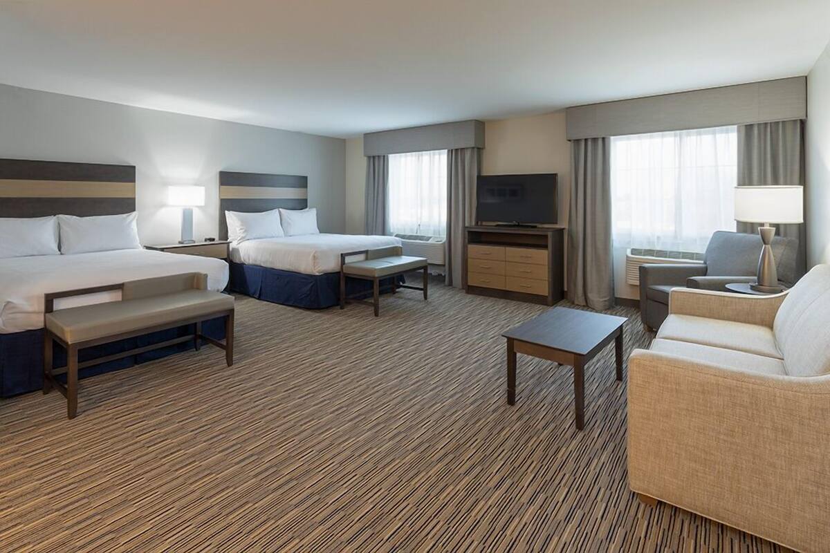 A hotel room with two beds, a sofa, a TV, a desk, and a lamp.