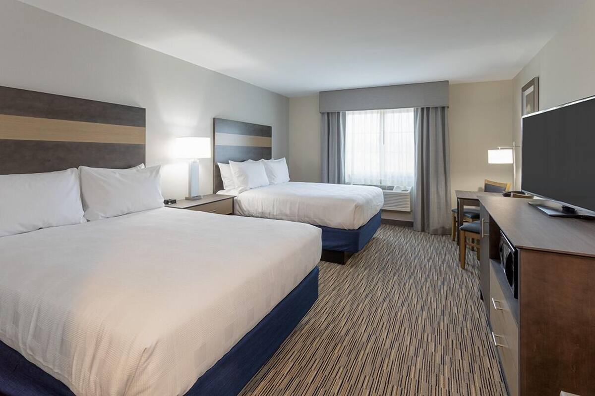 A hotel room with two beds, a desk with a chair, a television, and a large window with curtains.