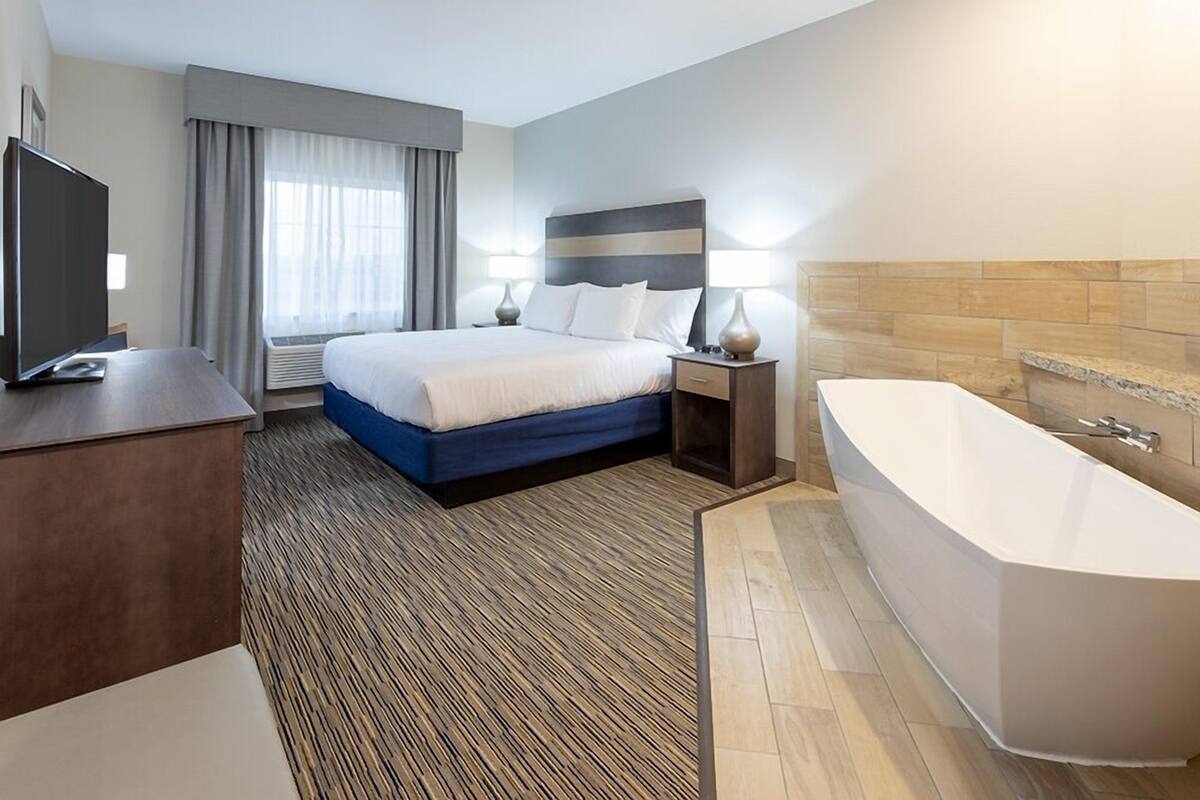 A hotel room with a bed, bedside lamps, a TV, a desk, and a bathtub.