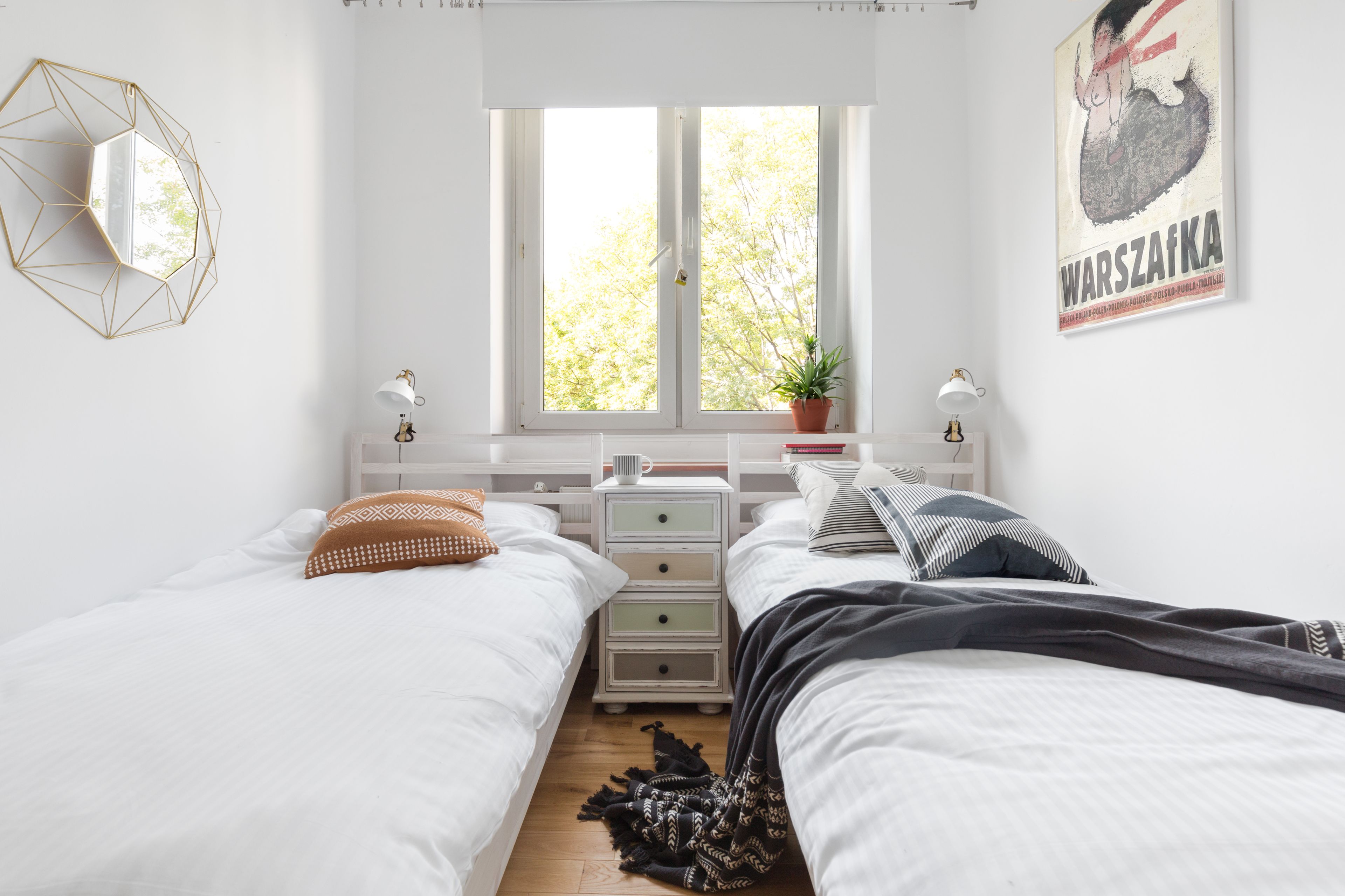 A bedroom with two beds, a window, a geometric wall decoration, a potted plant, and a poster on the wall.