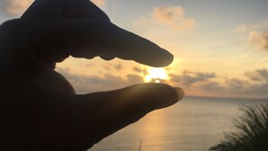 Eine Hand mit gespreizten Fingern, silhouettiert vor einem Sonnenuntergang über einem Gewässer.
