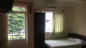 Ein Schlafzimmer mit Bett, einem fensterbelaubten Fenster, einer Klimaanlage und Blick ins Grüne.