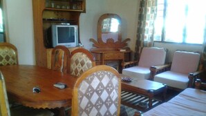 Een eetruimte met een houten tafel, stoelen, een televisietoestel en een spiegel.