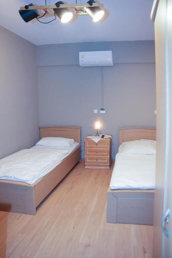 Quarto com duas camas de solteiro, mesa de cabeceira com luminária, ar-condicionado e luminária no teto.