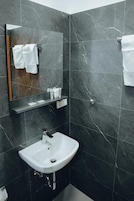 A modern bathroom with a white sink, dark marble walls, and a mirror with a towel rack.