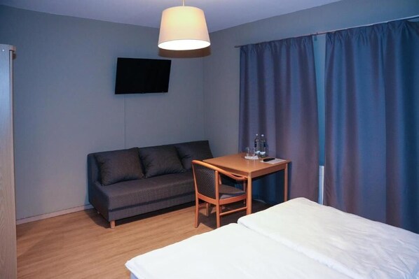 A hotel room with a bed, a desk, a chair, a sofa, a flat-screen TV, and a window with curtains. - Angelis Pension Frankfurt Airport (Kelsterbach)