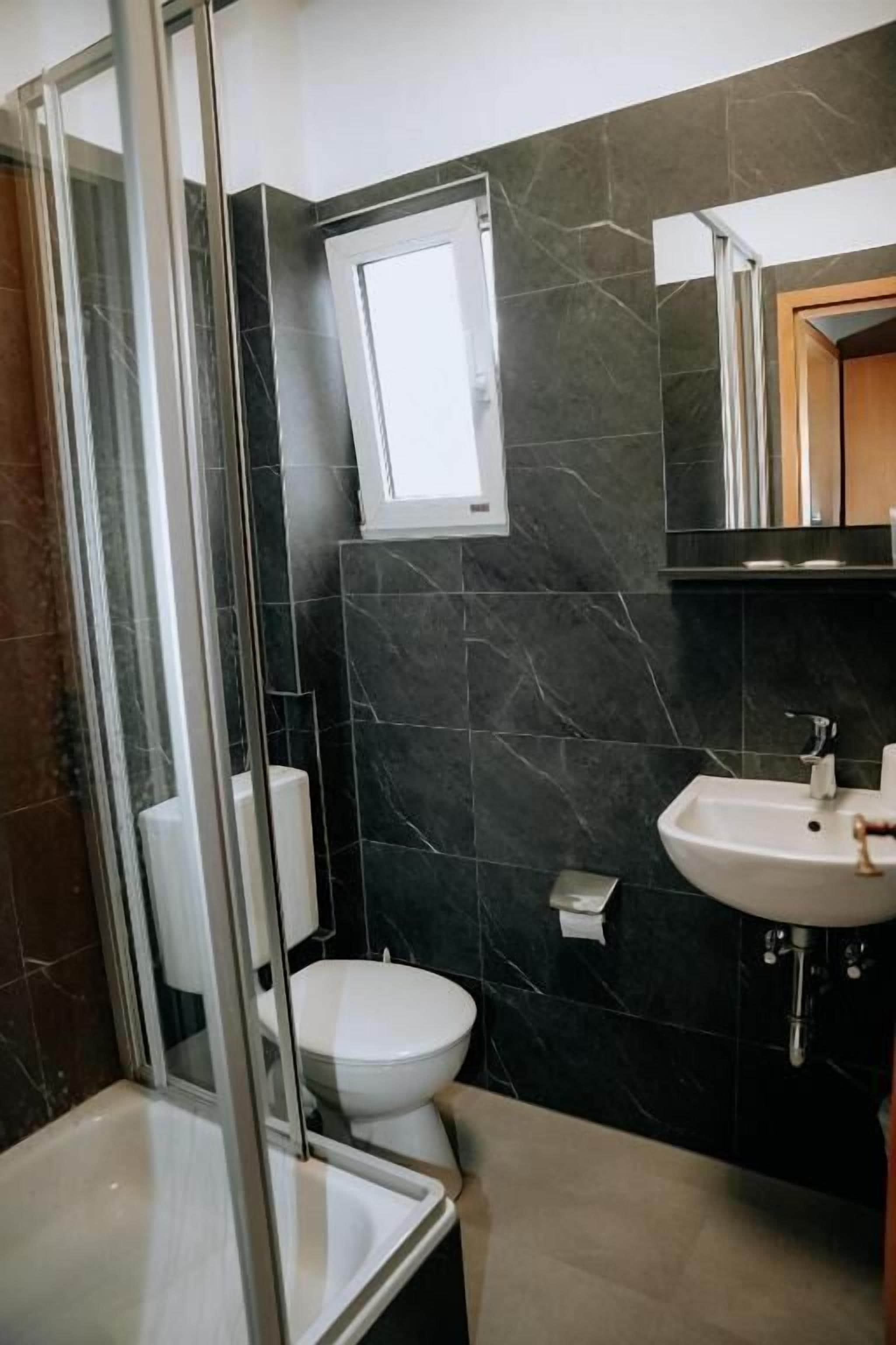 Ein Badezimmer mit Duschkabine aus Glas, Toilette, Waschbecken und Spiegel.