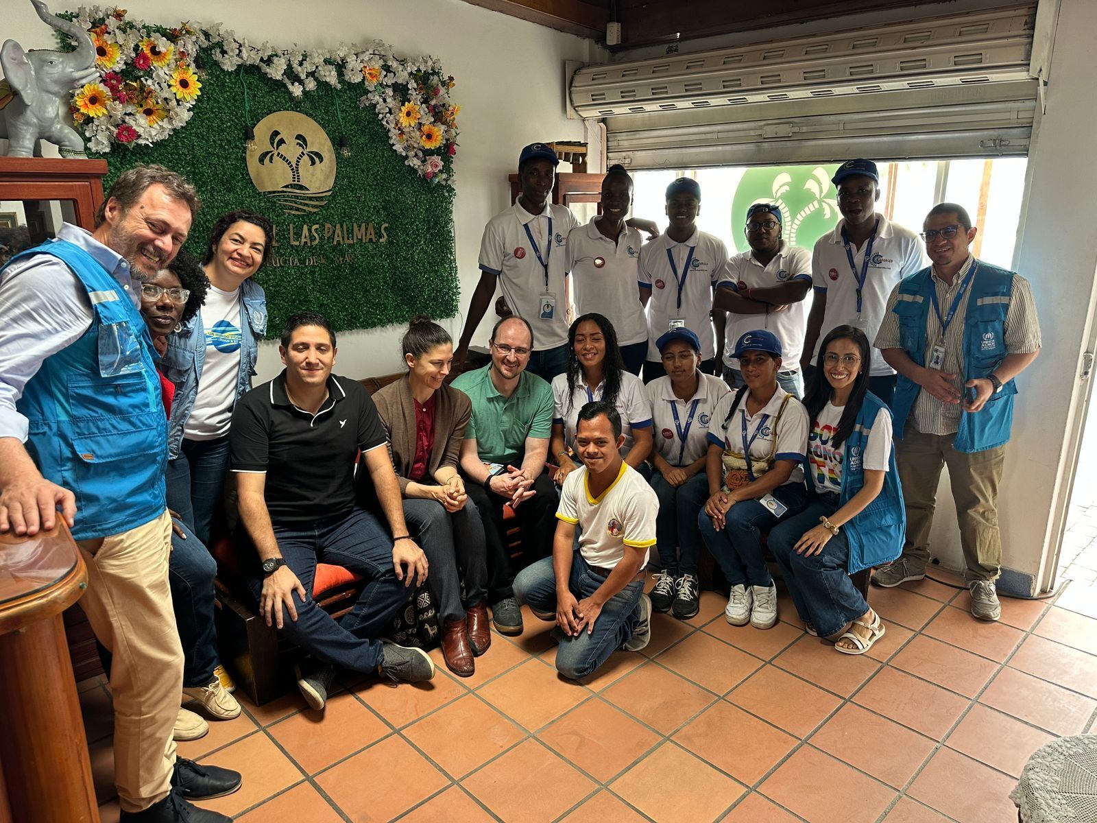 A group of people in a room with a green wall and a logo that reads "L'AS PALMAS".