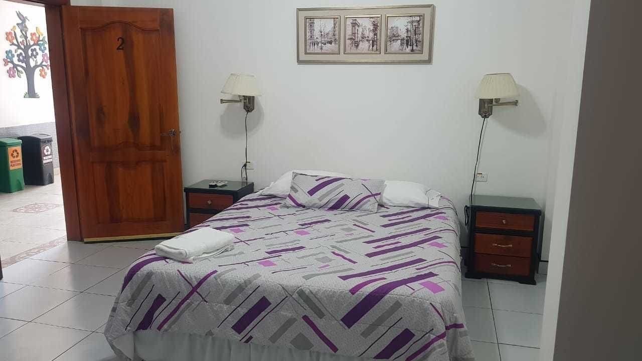 Un dormitorio con una cama, dos mesitas de noche, una puerta de madera y un cuadro colgado en la pared.