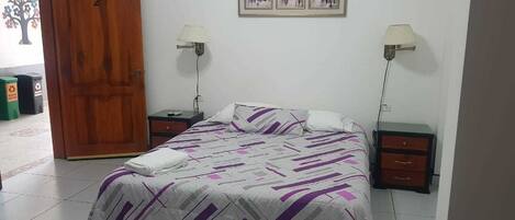 Un dormitorio con una cama, dos mesitas de noche, una puerta de madera y un cuadro colgado en la pared.