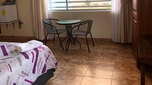 Una habitación de hotel con una cama, una pequeña mesa con sillas, un televisor montado en la pared y un ventanal con vista al mar.
