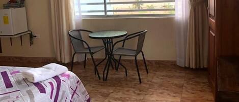 Una habitación de hotel con una cama, una pequeña mesa con sillas, un televisor montado en la pared y un ventanal con vista al mar.