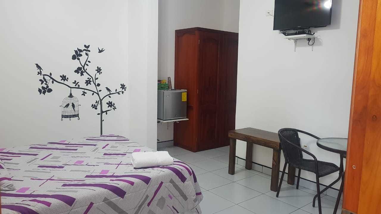 A bedroom with a bed, a desk, a chair, a wardrobe, and a TV mounted on the wall.