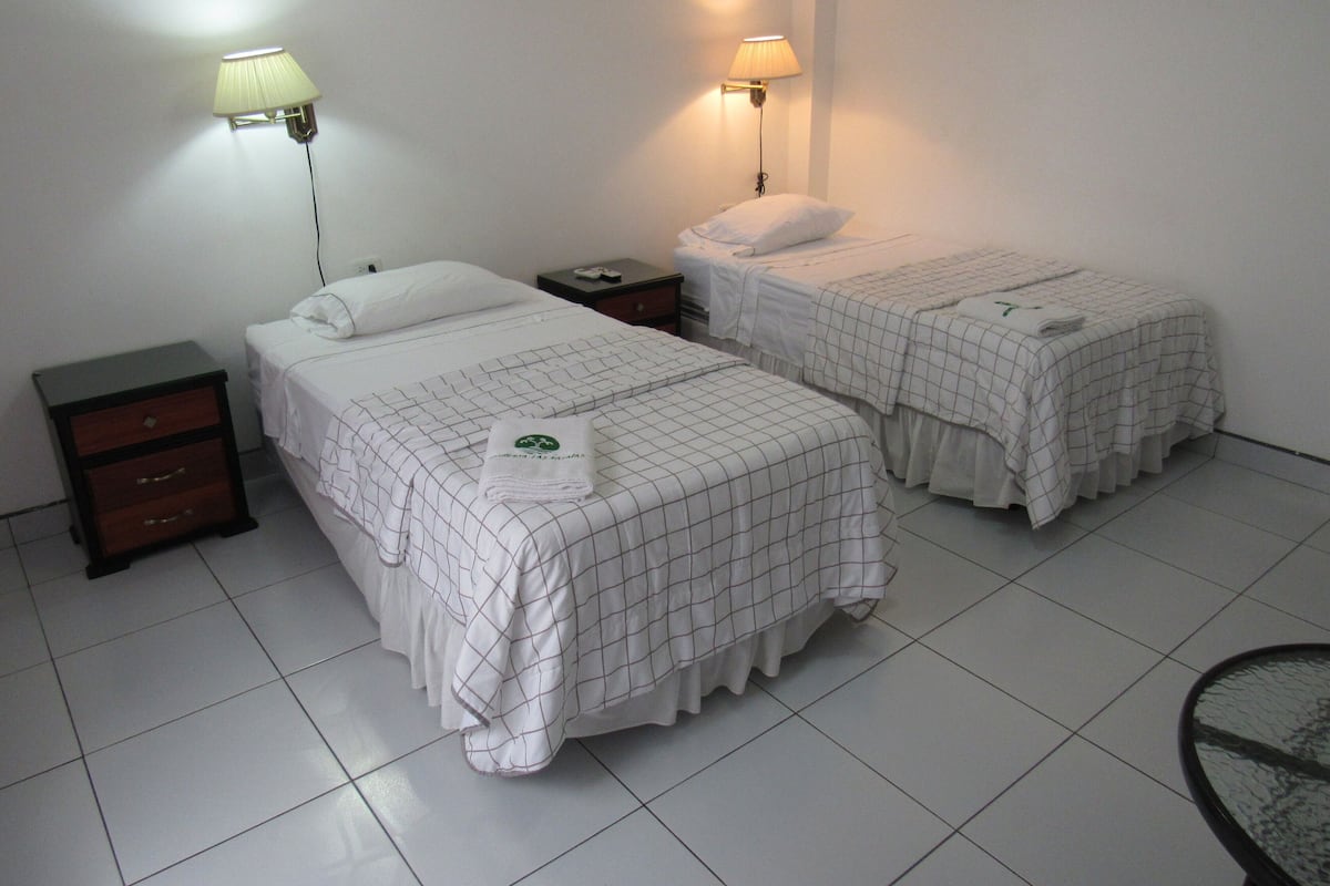 A hotel room with two beds, a nightstand, a lamp, and a chair.