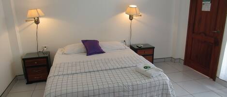 Una cama bien hecha con una colcha a cuadros, dos lámparas de noche, una almohada morada y una toalla doblada en el suelo.