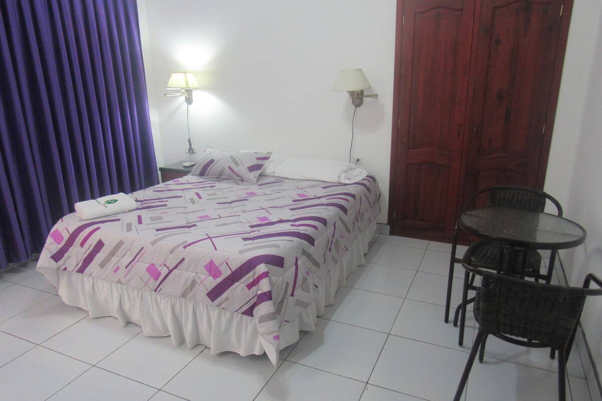A room with a bed, two wall-mounted lamps, a wooden door, and a small round table with chairs.