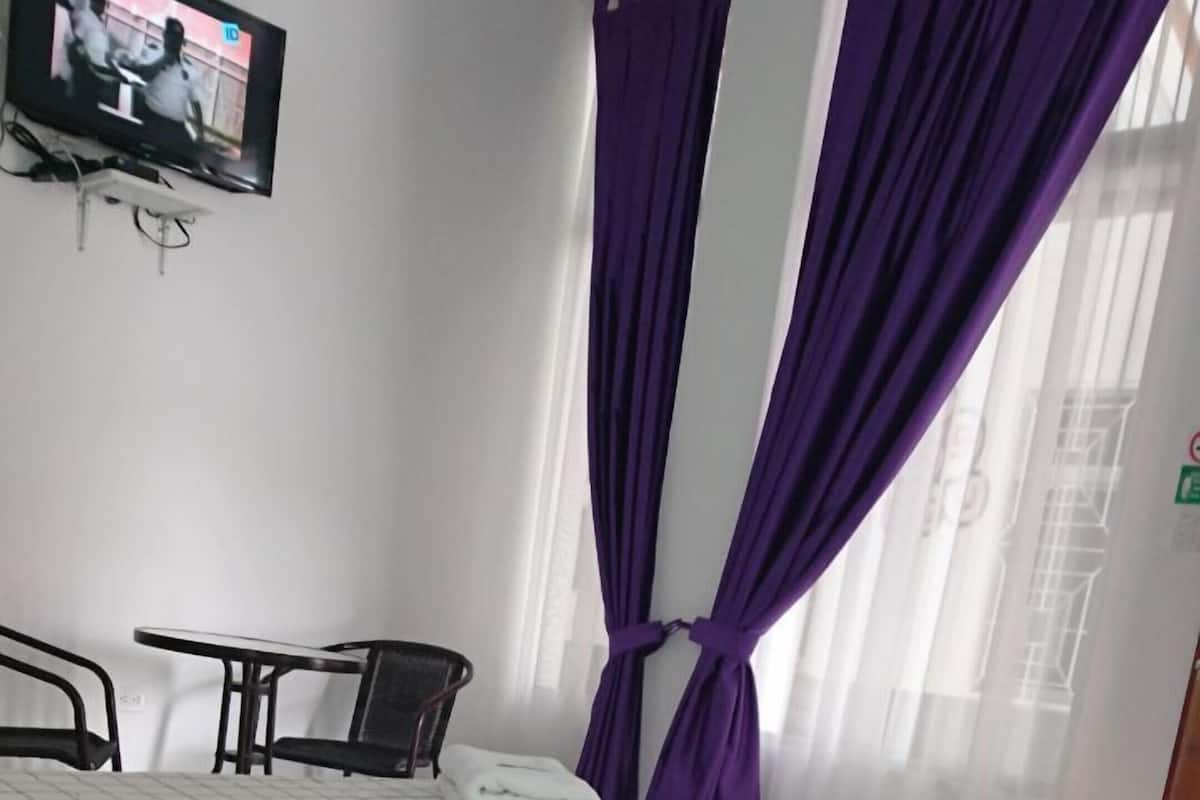 A hotel room with a bed, a chair, a TV, and purple curtains.