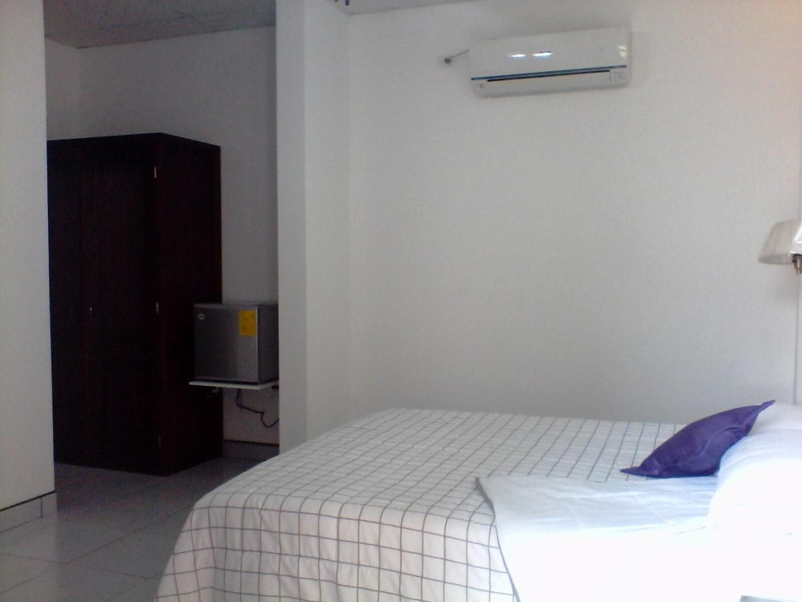 A bedroom with a bed, a wardrobe, and an air conditioning unit on the wall.