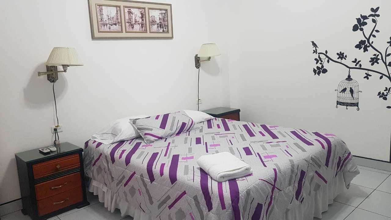 A neatly made bed with a patterned bedspread, a bedside table with a lamp, and a wall decoration of a birdcage.