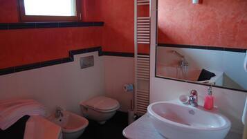 A bathroom with a toilet, bidet, sink, and a towel rack.