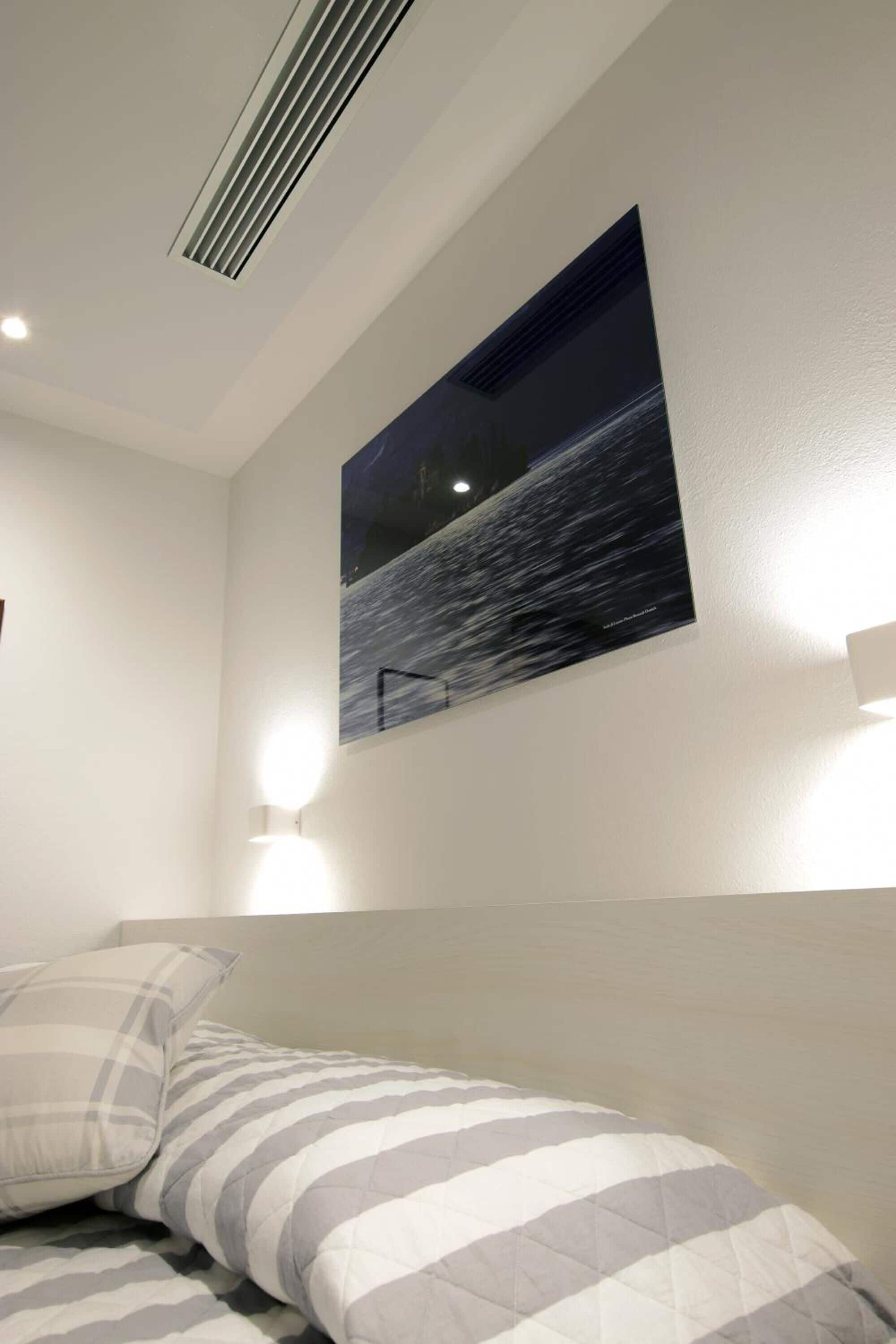Une chambre à coucher avec un lit, un tableau accroché au mur et une bouche d’aération au plafond.