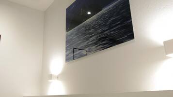 Une chambre à coucher avec un lit, un tableau accroché au mur et une bouche d’aération au plafond.