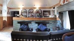 A bar area with a stone counter, two leather sofas with blue cushions, and a fireplace.
