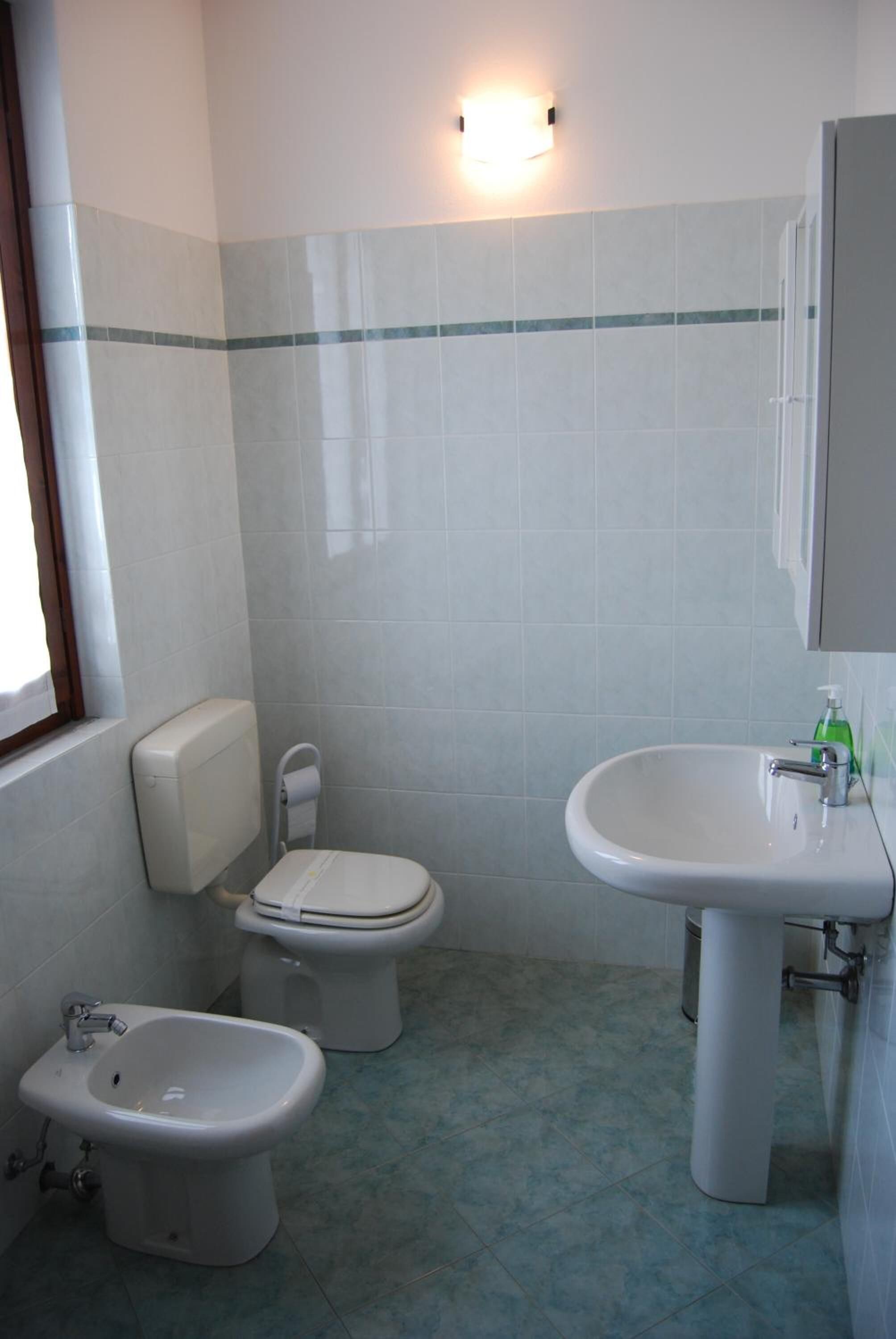 A bathroom with a toilet, bidet, sink, and a window.